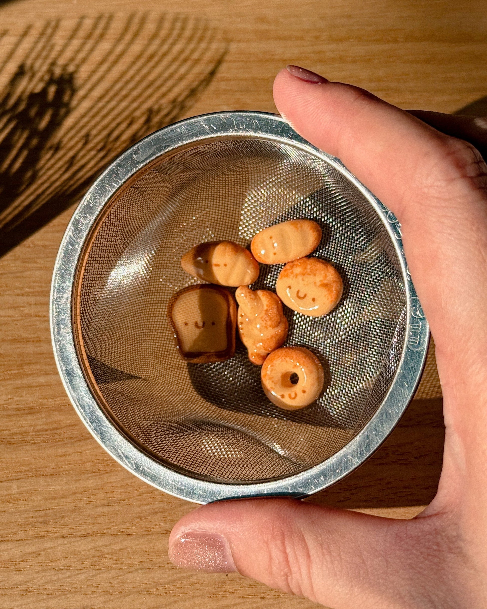Hand holding a metal strainer with small round objects on a wooden surface