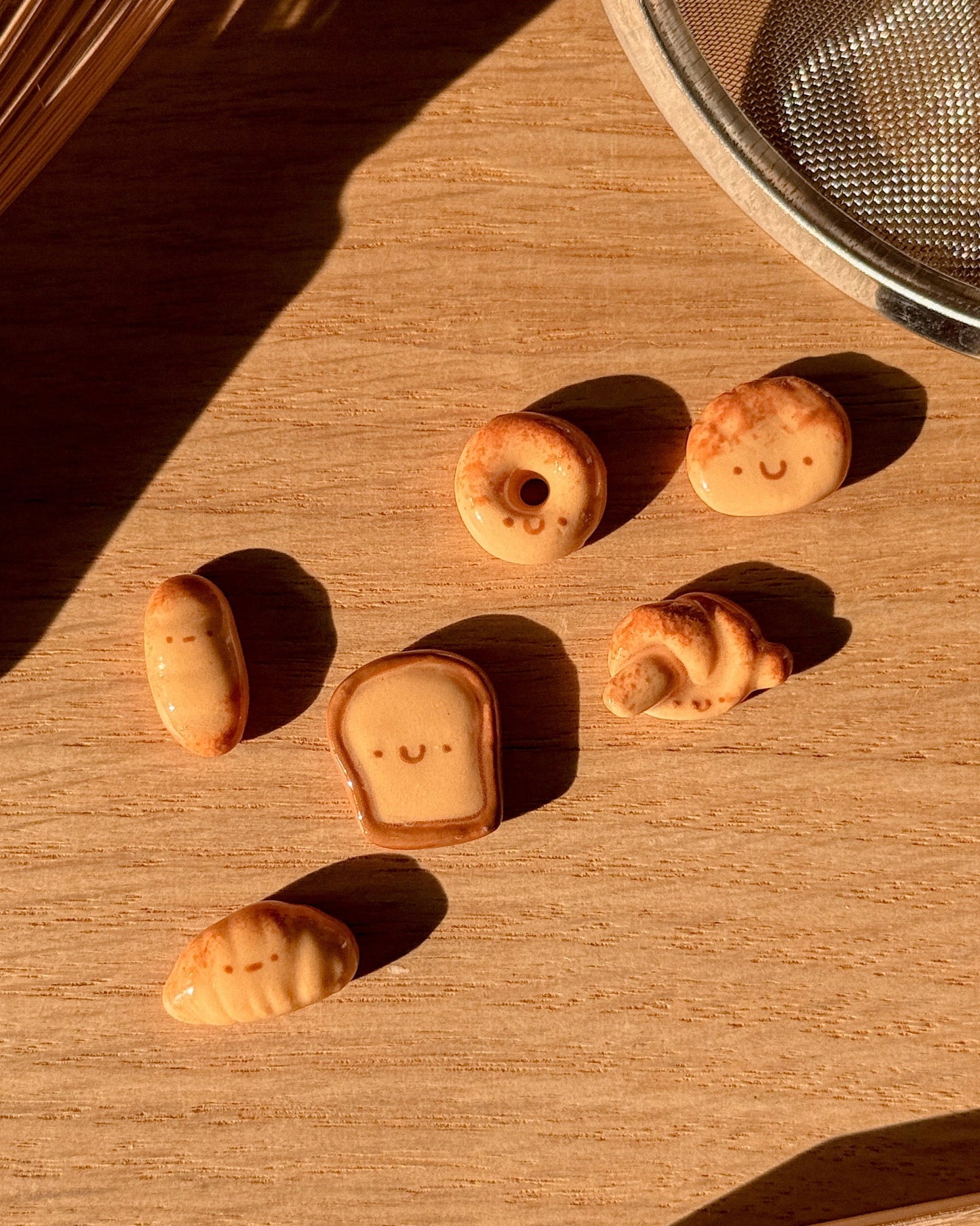Small croissant-shaped pastries on a wooden surface with a metal sieve in the background.